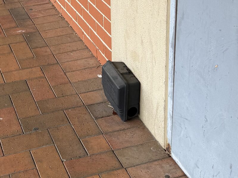 Rodent bait station installed at a commercial shopping strip entrance